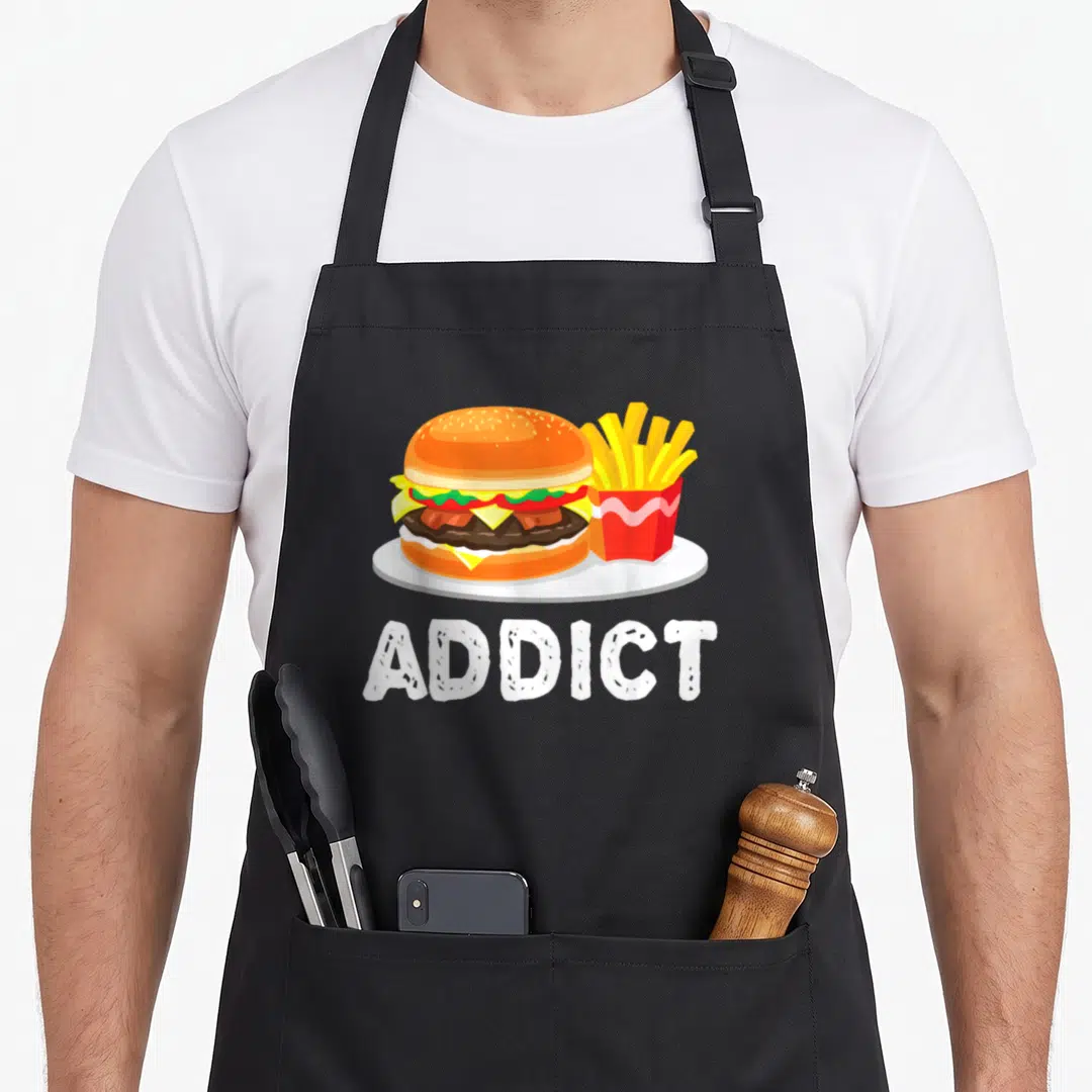 Bacon french apron - Cartoon burger and fries illustration above white ADDICT text — shown on a black cotton canvas apron against a white background