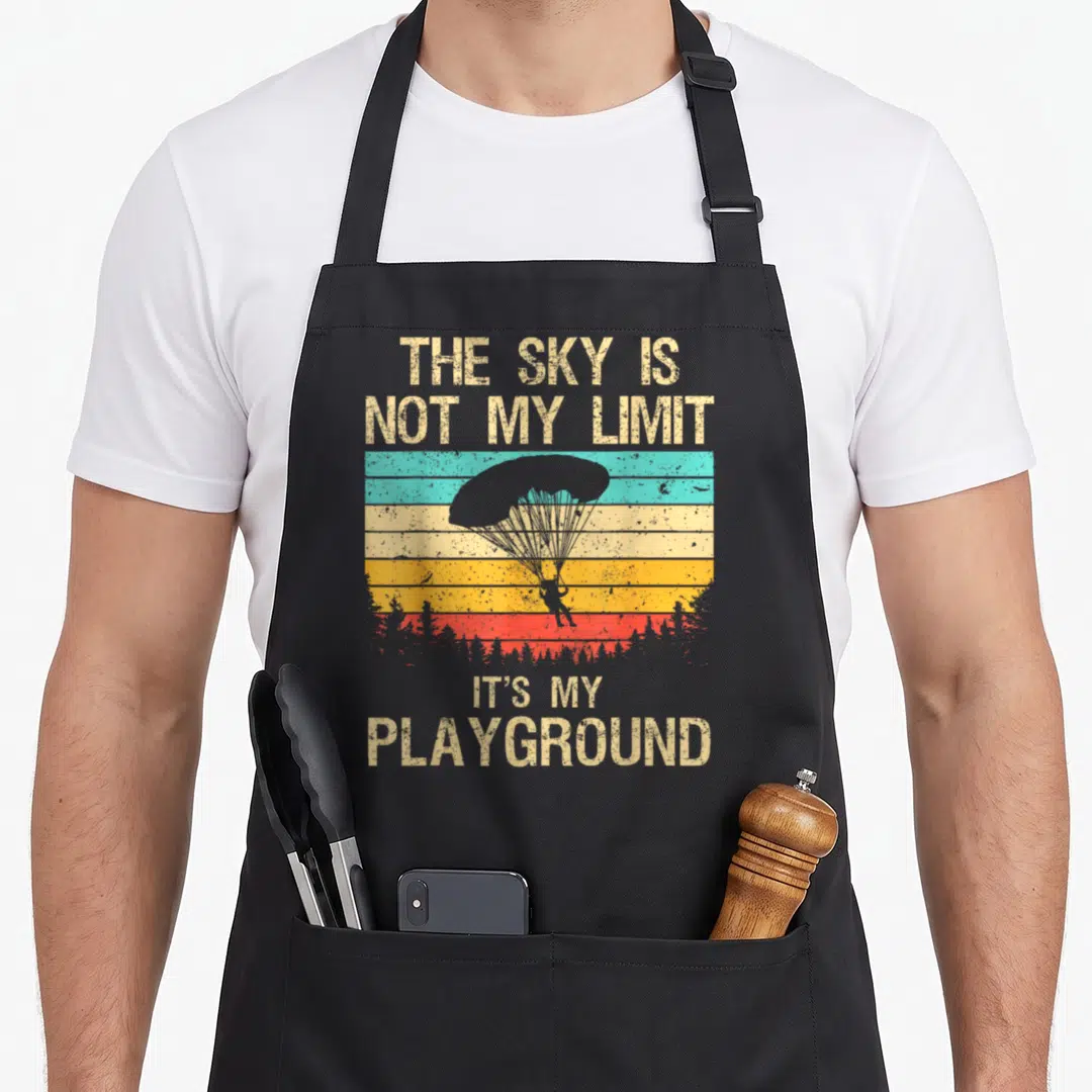 Skydive parachute apron - Retro parachutist silhouette on beige teal yellow orange red stripes with text The Sky Is Not — shown on a black cotton canvas apron against a white background