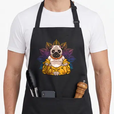 Pug meditation buddhist apron - Cartoon pug in yellow robe and orange beads sitting before a blue and orange mandala — shown on a black cotton canvas apron against a white background