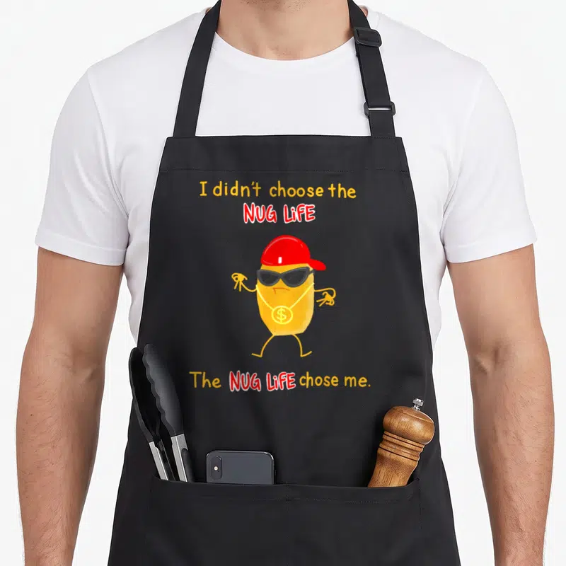 Didnt chicken print apron - Cartoon nugget red cap sunglasses gold dollar chain yellow red orange text — shown on a black cotton canvas apron against a white background