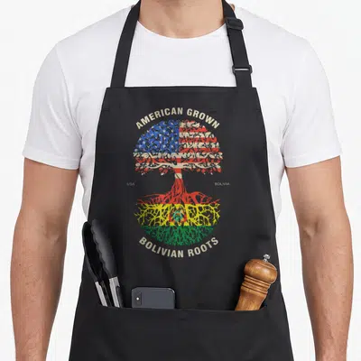 Grown bolivian american flag apron - Tree with US flag canopy and Bolivian flag roots and heritage text — shown on a black cotton canvas apron against a white background