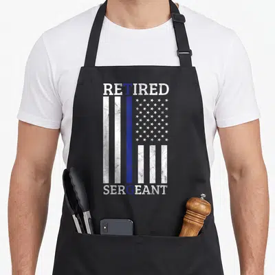 Sergeant american flag apron - Vertical distressed flag with blue stripe and RETIRED SERGEANT text — shown on a black cotton canvas apron against a white background