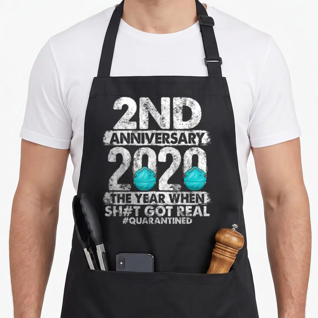 Anniversary 2nd apron - Stacked white text reading 2nd Anniversary 2020 with two teal face masks covering the zeros — shown on a black cotton canvas apron against a white background