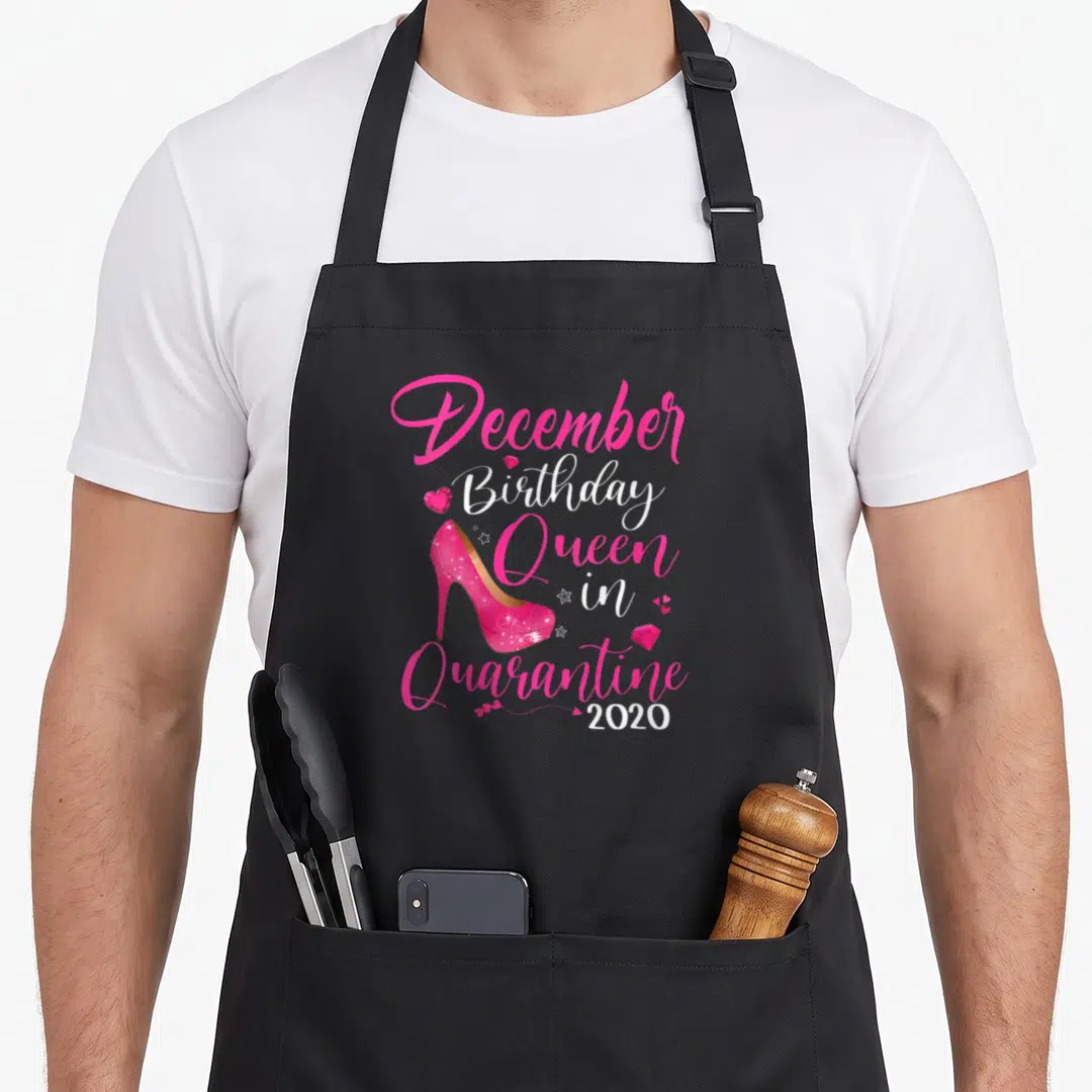 December quarantine birthday apron - Pink high heel shoe and stacked text reading December Birthday Queen in Quarantine — shown on a black cotton canvas apron against a white background