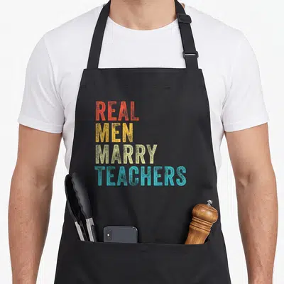 Future teacher pocket apron - Stacked text reading Real Men Marry Teachers in red yellow beige and blue block letters — shown on a black cotton canvas apron against a white background