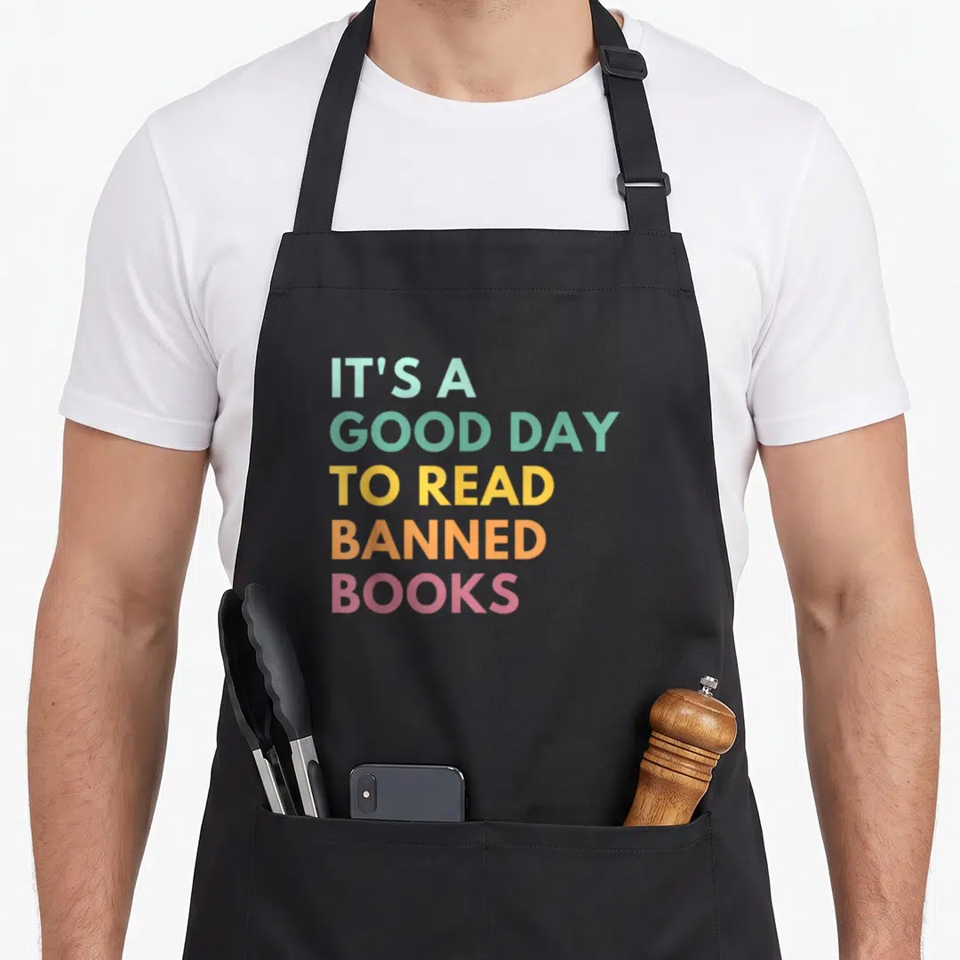 Read cute bookworm and library worker apron - Stacked colorful text reading It's A Good Day To Read Banned Books — shown on a black cotton canvas apron against a white background