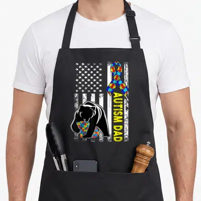 Autism father day apron - Black bear hugging puzzle cub on distressed US flag with vertical yellow text — shown on a black cotton canvas apron against a white background