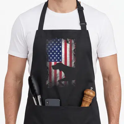 Patriotic pointer apron - Grey dog silhouette over distressed red white and blue American flag — shown on a black cotton canvas apron against a white background