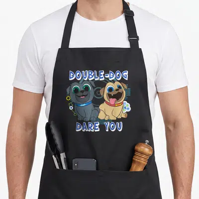 Puppy double apron - Two cartoon pugs with DOUBLE-DOG DARE YOU text and tech icons — shown on a black cotton canvas apron against a white background