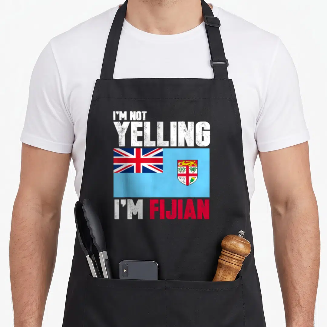 Yelling fiji apron - I'M NOT YELLING I'M FIJIAN text flanking a distressed flag of Fiji in blue red and white — shown on a black cotton canvas apron against a white background