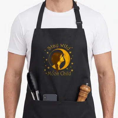 Wild hippie apron - Gold woman profile inside crescent moon with stars and arched text — shown on a black cotton canvas apron against a white background