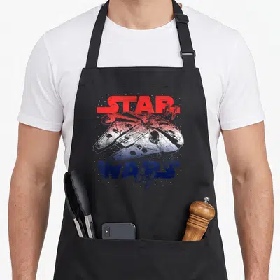 July falcon apron - Red white blue distressed Star Wars text with Millennium Falcon and TIE fighters — shown on a black cotton canvas apron against a white background
