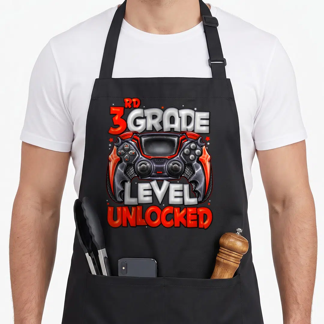 Unlocked game aprons - Red black and white game controller with RD 3 GRADE LEVEL UNLOCKED text and stars — shown on a black cotton canvas apron against a white background