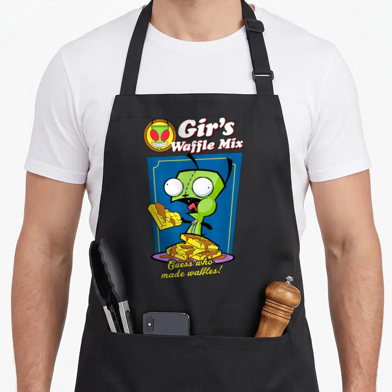 Invader waffles apron - Gir holding a waffle inside a blue box with Gir's Waffle Mix text — shown on a black cotton canvas apron against a white background