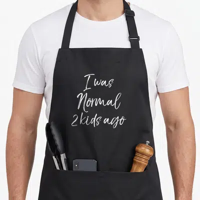 Normal mother's day aprons - White I was Normal 2 kids ago script text on black background — shown on a black cotton canvas apron against a white background