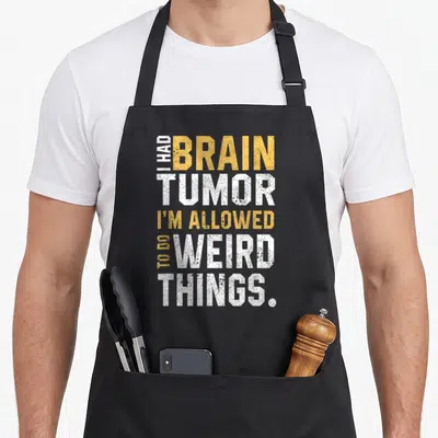 Tumor aneurysm awareness apron - Yellow and white stacked text I Had Brain Tumor I'm Allowed To Do Weird Things on gray — shown on a black cotton canvas apron against a white background