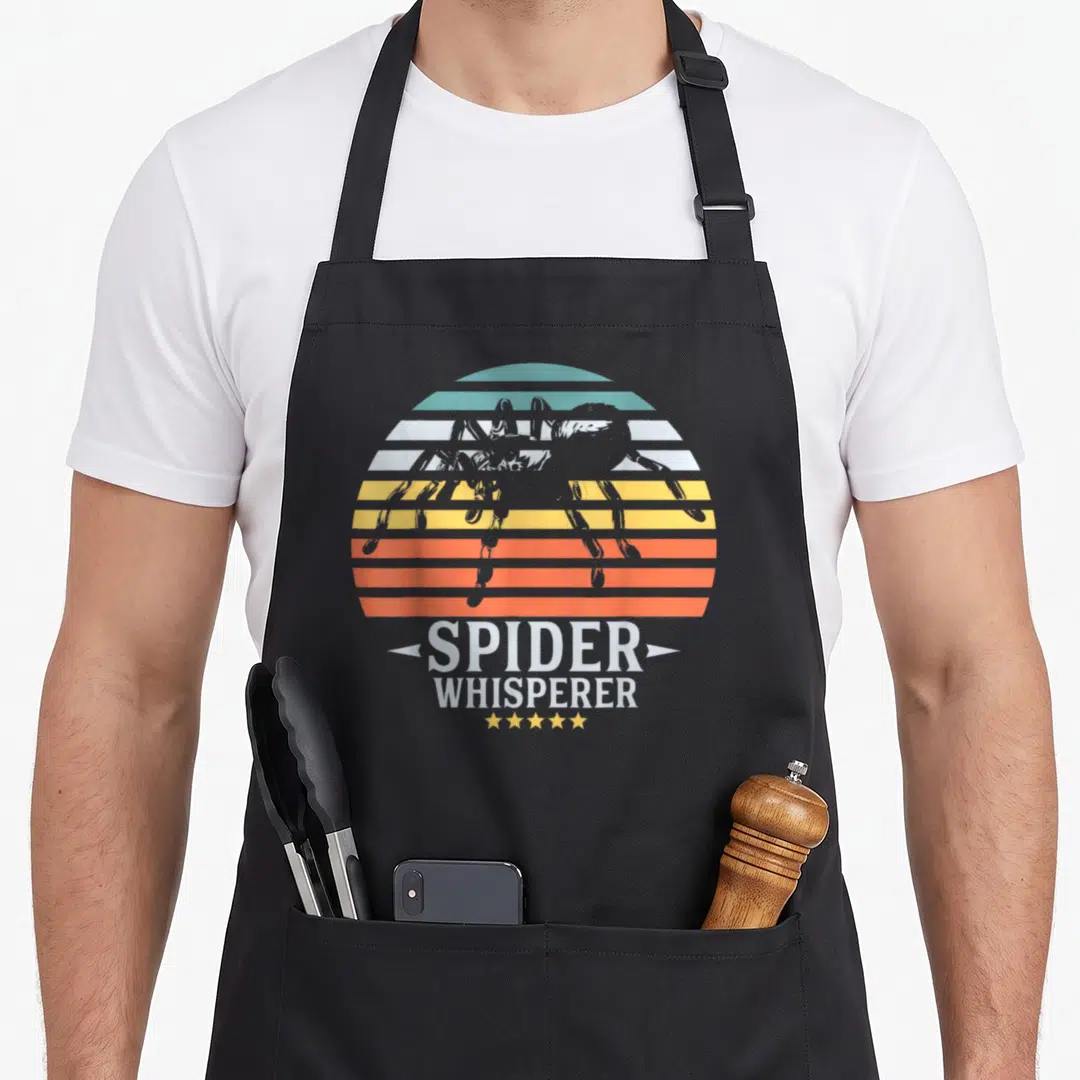 Whisperer halloween apron - Retro striped sun with spider silhouette and SPIDER WHISPERER text — shown on a black cotton canvas apron against a white background