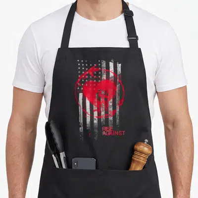 Rise stained apron - Distressed USA flag with red heart, paint circle, and RISE AGAINST text in red and white — shown on a black cotton canvas apron against a white background