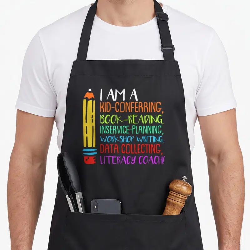 Coach literacy apron - Cartoon pencil with seven lines of colored text listing literacy coach duties — shown on a black cotton canvas apron against a white background