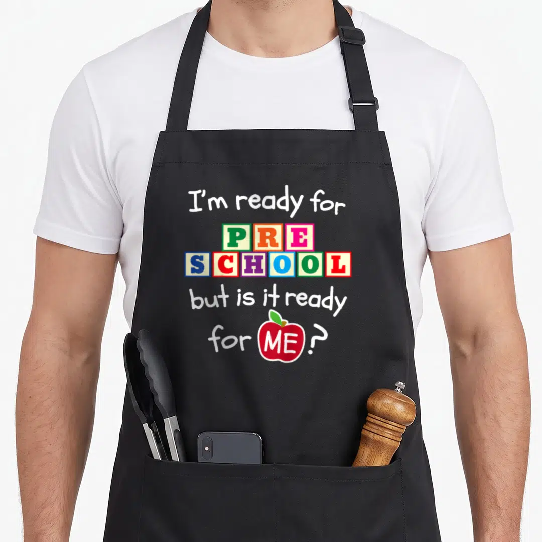 Hello preschool apron - Stacked text in toy blocks reading PRE SCHOOL above red apple containing word ME — shown on a black cotton canvas apron against a white background