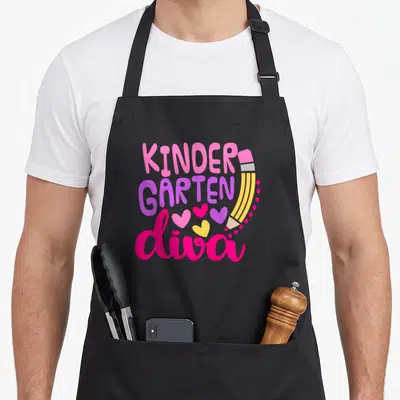Kindergarten diva apron - Stacked KINDER GARTEN diva text with yellow pencil and three hearts in pink purple yellow — shown on a black cotton canvas apron against a white background