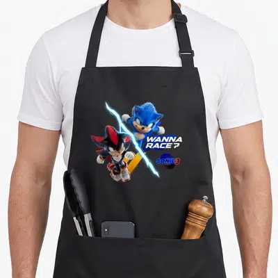 Race crazy hedgehog man apron - Sonic and rival separated by lightning bolt with WANNA RACE? text in blue and red — shown on a black cotton canvas apron against a white background