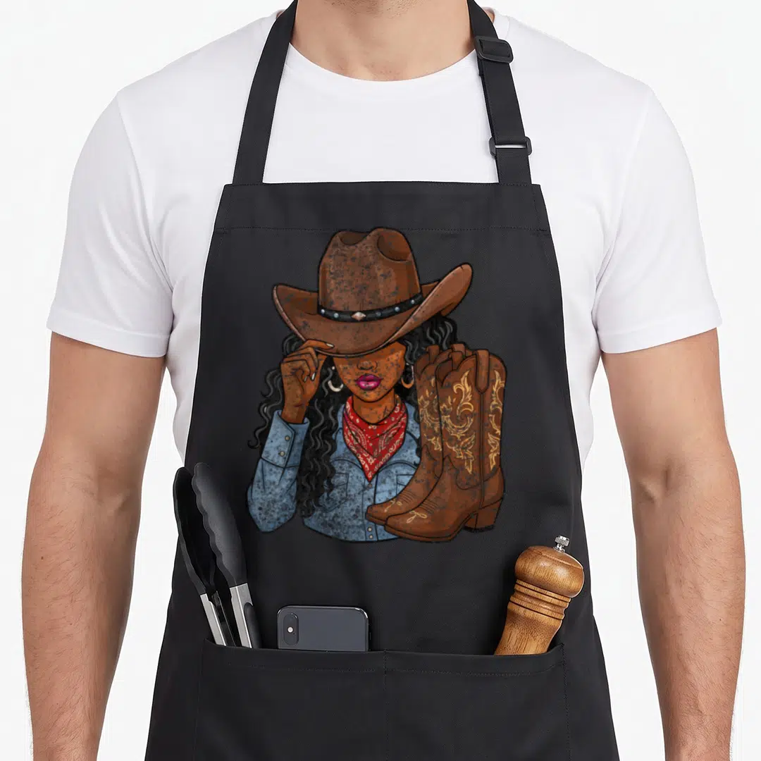 Cowgirl western aprons - Cartoon woman in brown hat and red bandana beside brown boots with gold embroidery — shown on a black cotton canvas apron against a white background