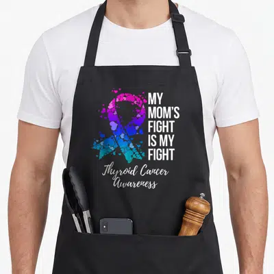 Fight cancer thyroid apron - Heart ribbon in pink purple blue with My Moms Fight Is My Fight text — shown on a black cotton canvas apron against a white background