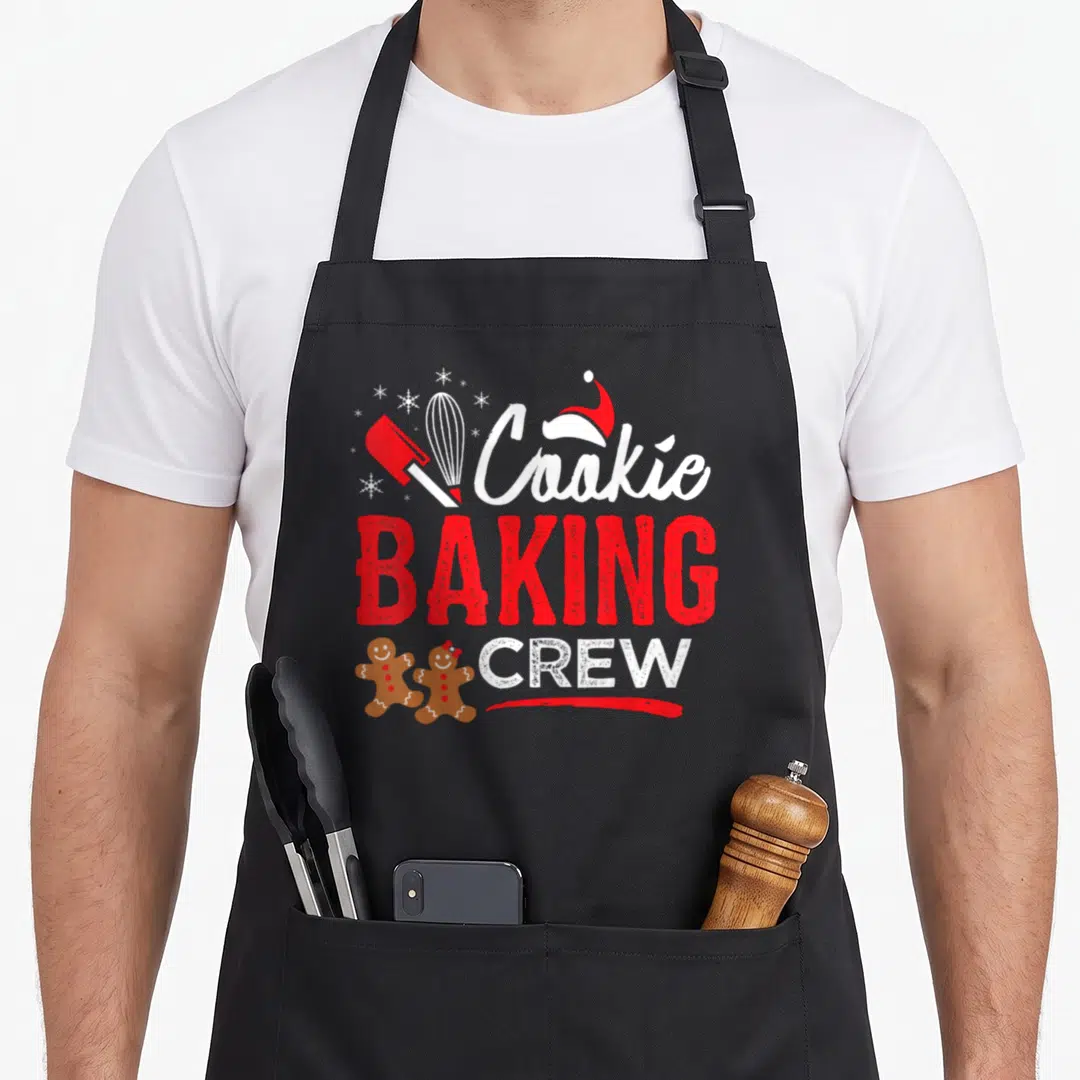 Crew christmas holiday baking apron - Cookie Baking Crew text with spatula whisk gingerbread men and santa hat in red — shown on a black cotton canvas apron against a white background
