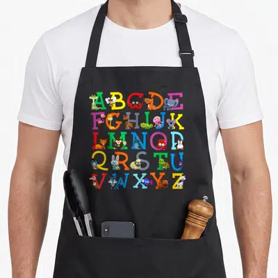 Letter animal apron - A-Z alphabet grid with cartoon bee elephant zebra in green blue red yellow pink — shown on a black cotton canvas apron against a white background