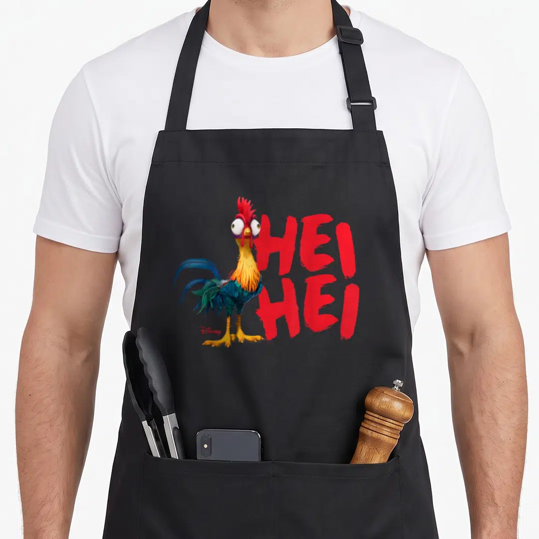 Character rooster apron - Cartoon rooster with red comb and blue tail feathers beside red HEI HEI text — shown on a black cotton canvas apron against a white background