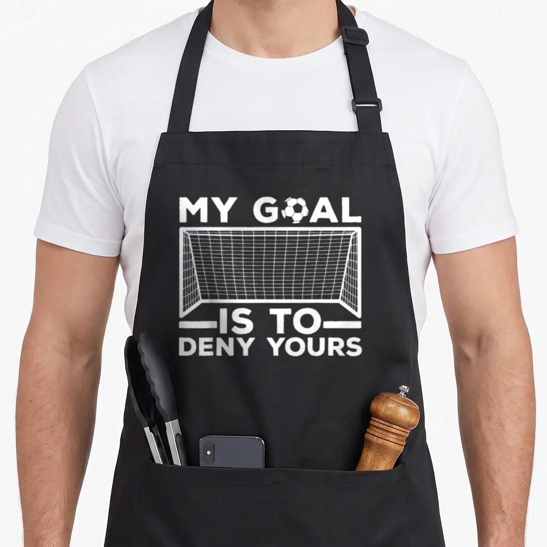 Defender funny soccer apron - White soccer goal graphic with text My Goal Is To Deny Yours and a ball replacing — shown on a black cotton canvas apron against a white background