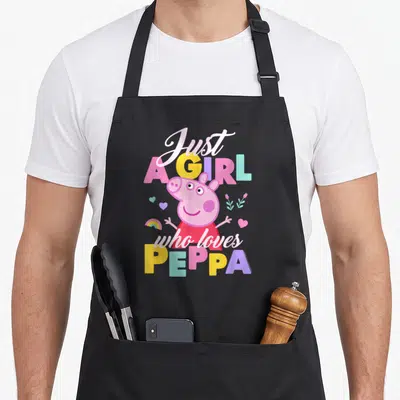 Playing pig apron - Just A GIRL who loves PEPPA cartoon text with pink character and scattered hearts flowers rainbow — shown on a black cotton canvas apron against a white background