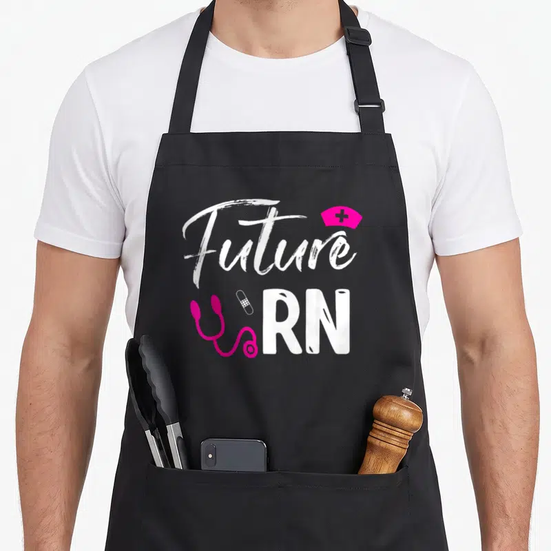 Future registered nurse apron - White Future RN text with pink stethoscope bandage and nurse cap — shown on a black cotton canvas apron against a white background