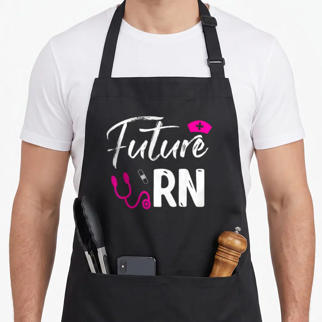 Future registered nurse apron - White Future RN text with pink stethoscope bandage and nurse cap — shown on a black cotton canvas apron against a white background