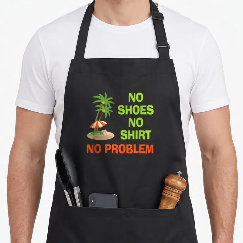 Shoe kitchen island apron - Cartoon palm tree with striped chair and stacked text NO SHOES NO SHIRT NO PROBLEM — shown on a black cotton canvas apron against a white background