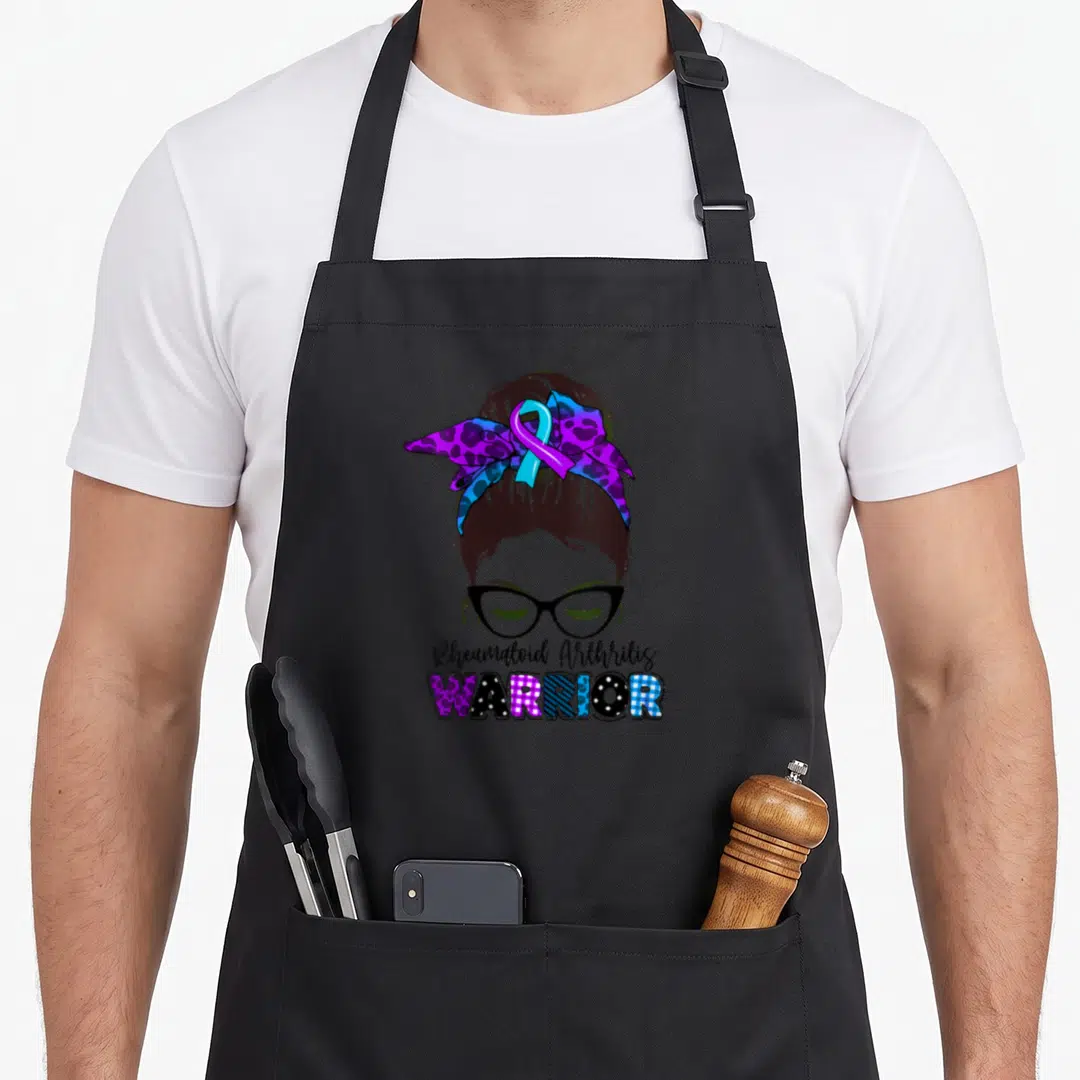 Arthritis messy aprons - Cartoon woman bun bow glasses Rheumatoid Arthritis WARRIOR patterned letters purple blue brown — shown on a black cotton canvas apron against a white background