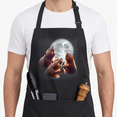 Howling beaver apron - Three realistic brown beavers howling at a large grey full moon — shown on a black cotton canvas apron against a white background