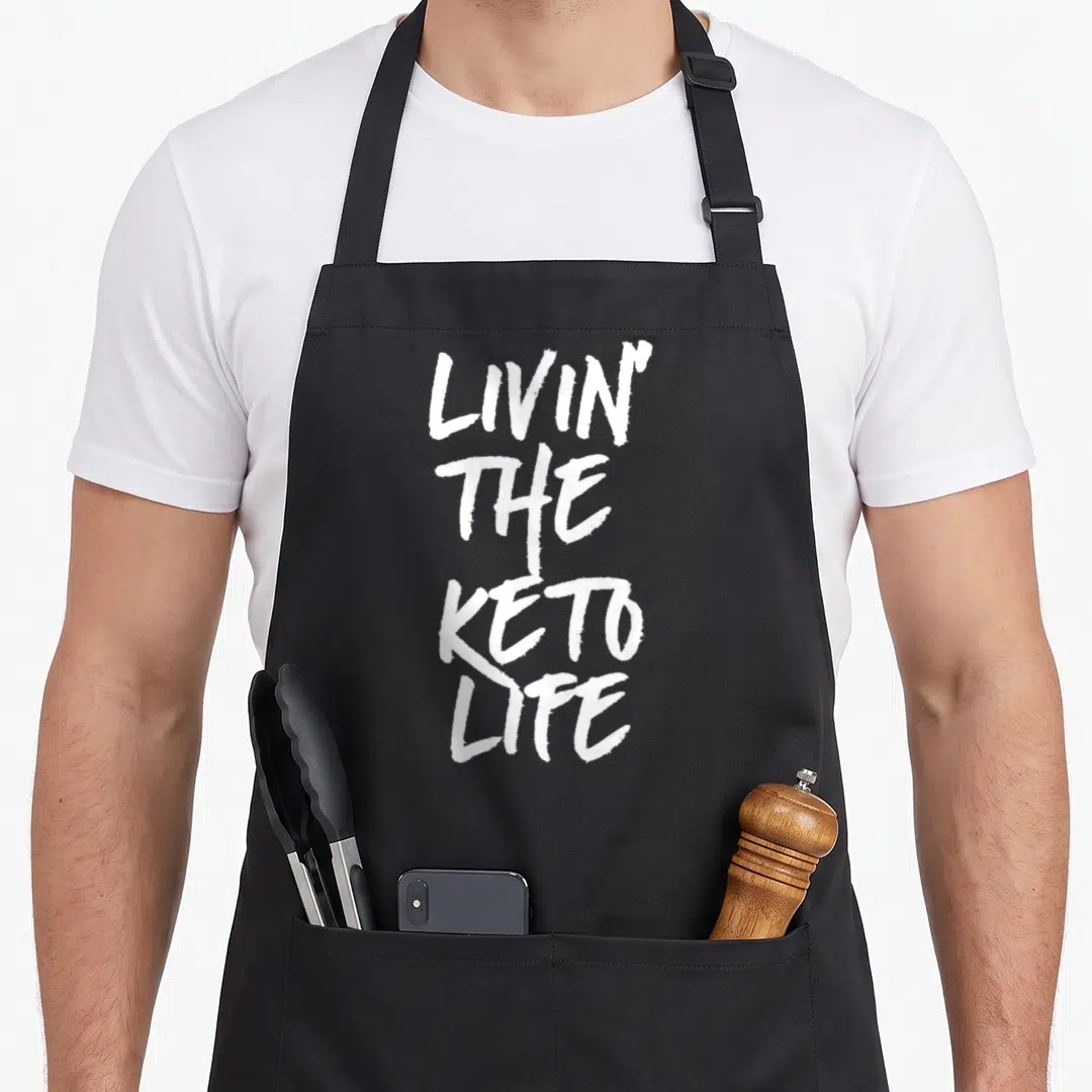 Livin son life apron - White stacked text reading LIVIN THE KETO LIFE on dark background — shown on a black cotton canvas apron against a white background