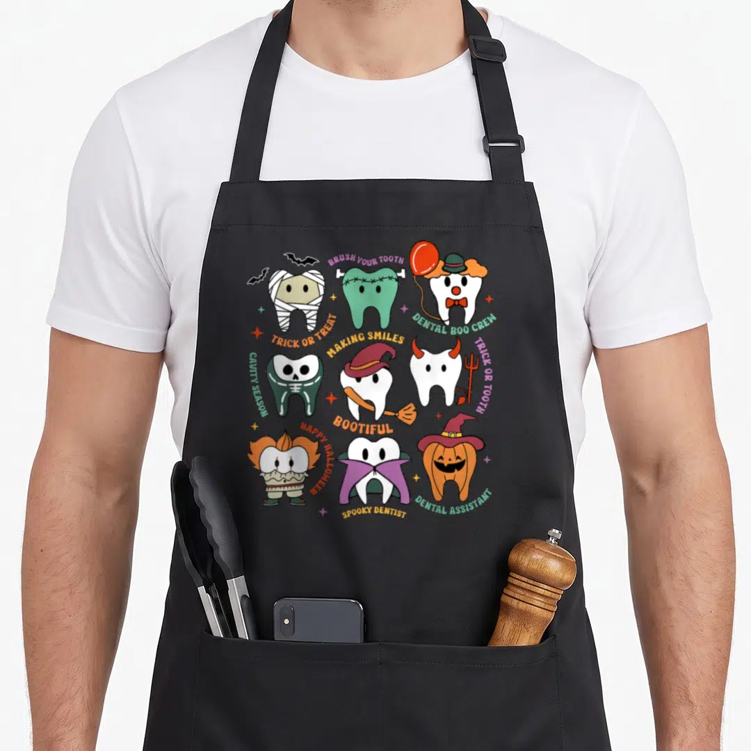 Boo dentist apron - Seven costumed cartoon teeth in orange, purple, green, and white surrounded by Halloween dental pun — shown on a black cotton canvas apron against a white background