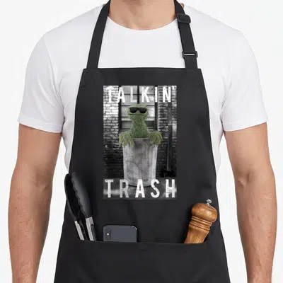 Talkin oscar the grouch apron - Green Oscar the Grouch in grey trash can with white Talkin Trash text on brick — shown on a black cotton canvas apron against a white background