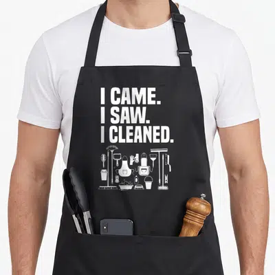 Cleaning cleaner housekeeper apron - White I CAME I SAW I CLEANED text above line art of broom gloves bucket — shown on a black cotton canvas apron against a white background
