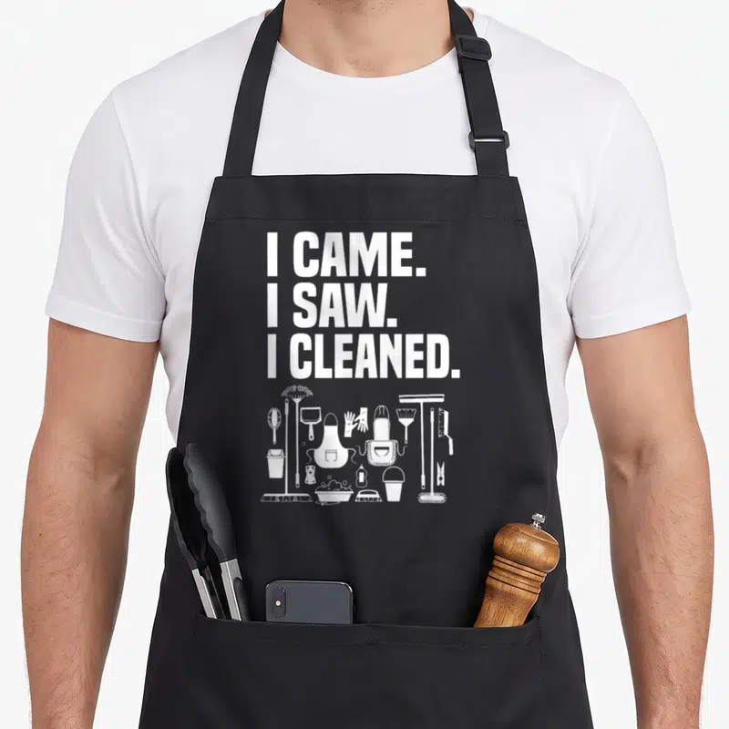 Cleaning cleaner housekeeper apron - White I CAME I SAW I CLEANED text above line art of broom gloves bucket — shown on a black cotton canvas apron against a white background