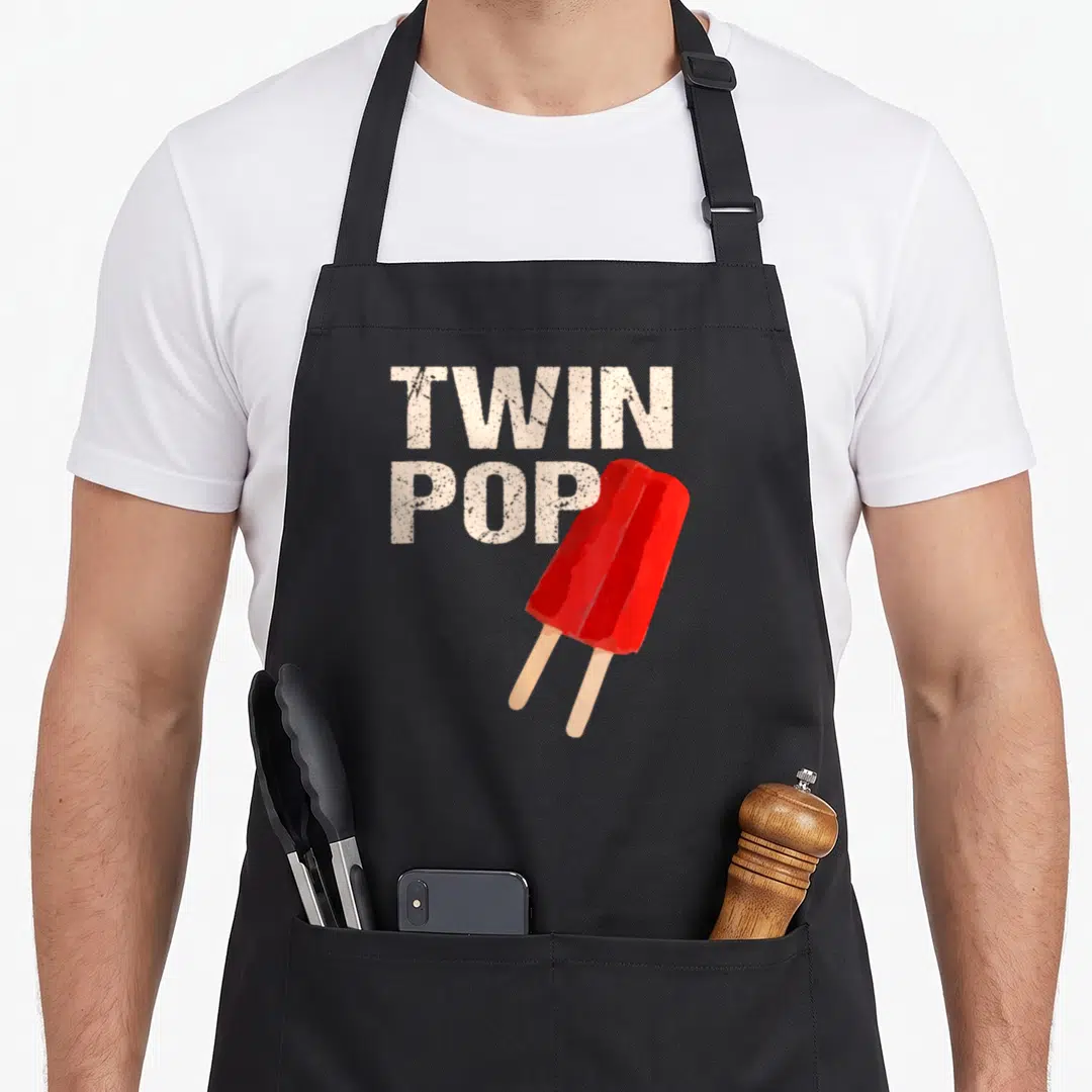 Twin father day apron - Red double-stick popsicle overlapping white TWIN POP text on black apron — shown on a black cotton canvas apron against a white background