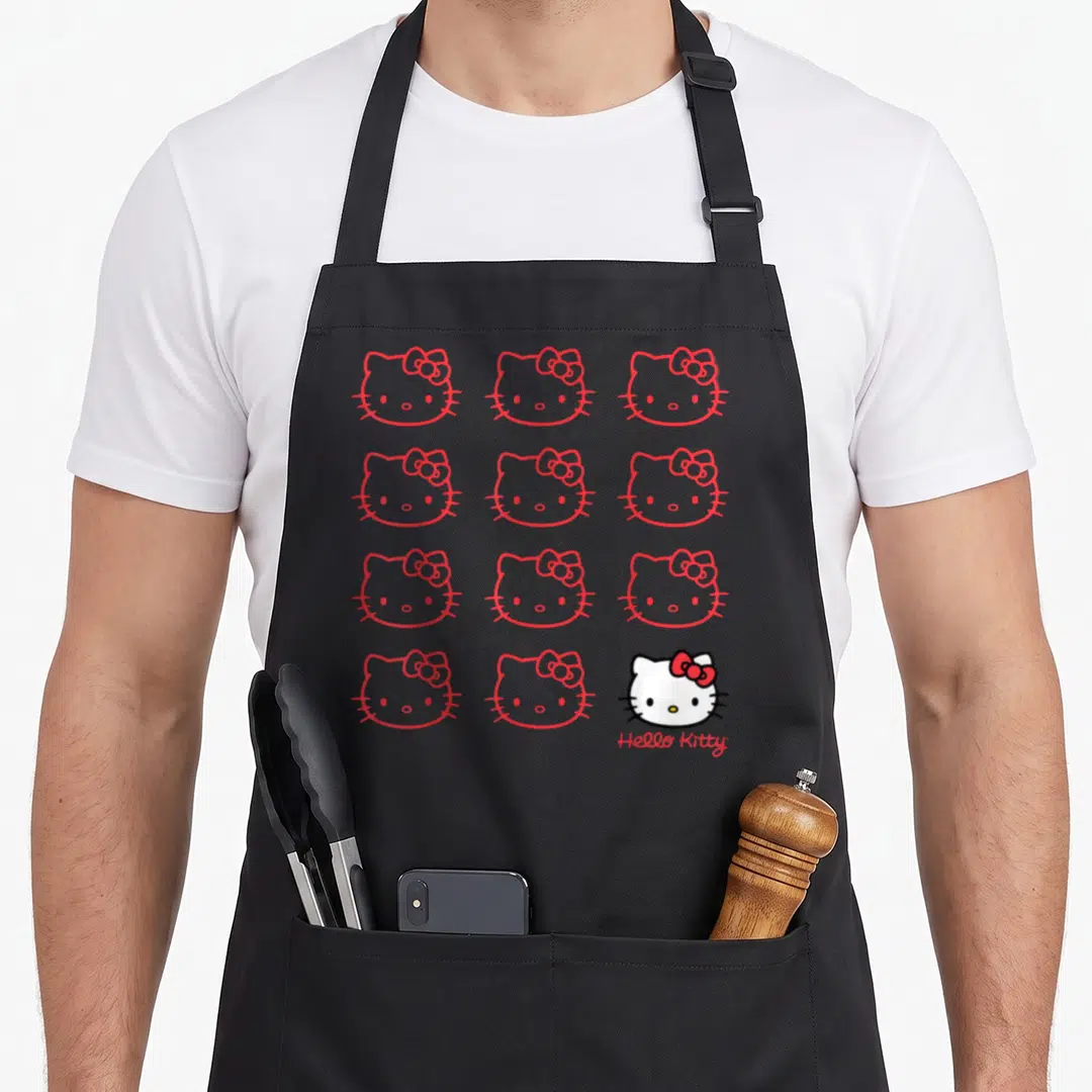Retro crew apron - Grid of red outline cat heads with one colored face and Hello Kitty text — shown on a black cotton canvas apron against a white background