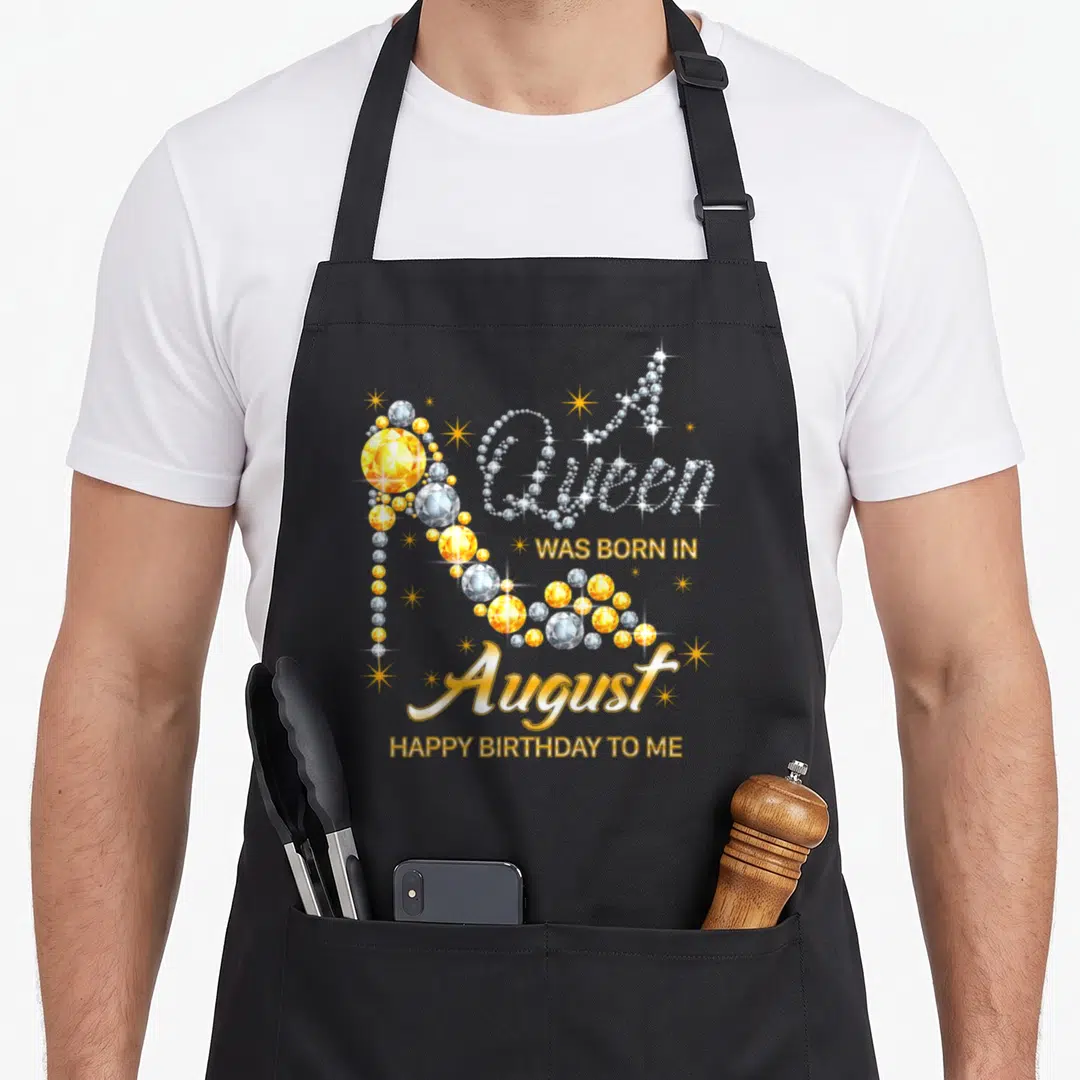 Funny queen august birthday apron - Diamond high heel shoe and A Queen was born in August text with yellow stars — shown on a black cotton canvas apron against a white background