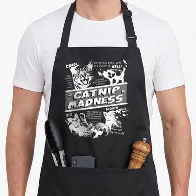 Catnip pet apron - Distressed white text and cat illustrations depicting feline madness and vice on a grey background — shown on a black cotton canvas apron against a white background