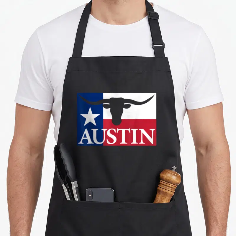Retro austin texas aprons - Longhorn steer silhouette over Texas flag with AUSTIN text in blue white red grey — shown on a black cotton canvas apron against a white background