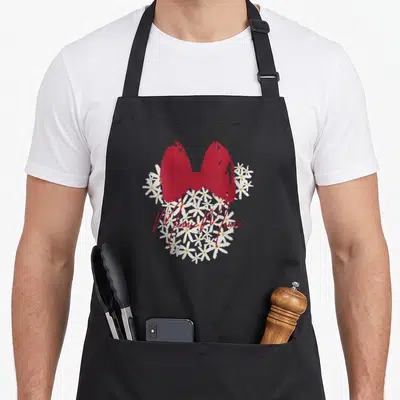 Floral easter apron - Minnie Mouse silhouette formed by white daisies with a red bow and script text — shown on a black cotton canvas apron against a white background