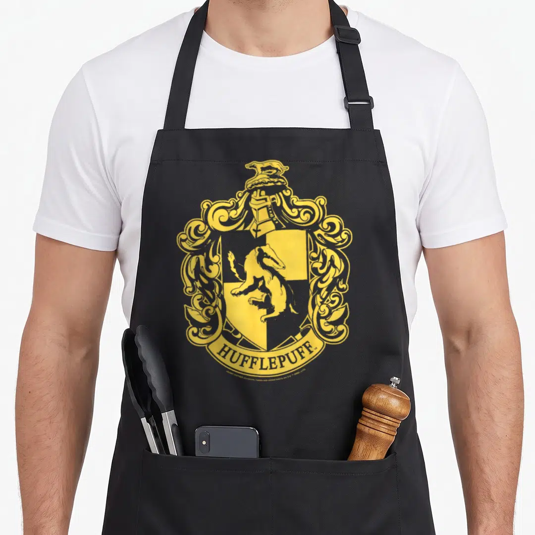 Hufflepuff simple apron - Yellow line-art crest with badger in shield, helmet, ornate mantling, and HUFFLEPUFF banner — shown on a black cotton canvas apron against a white background
